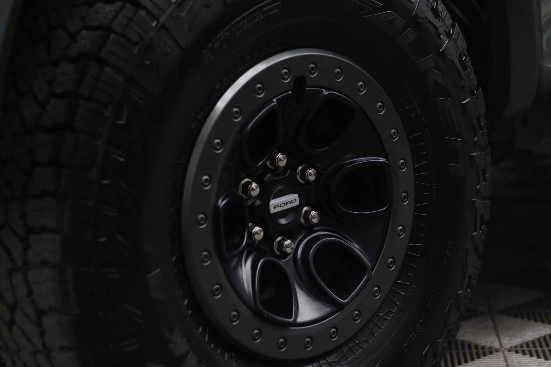 A person wearing black gloves uses a blue applicator sponge to apply product to the glossy black side of a car.