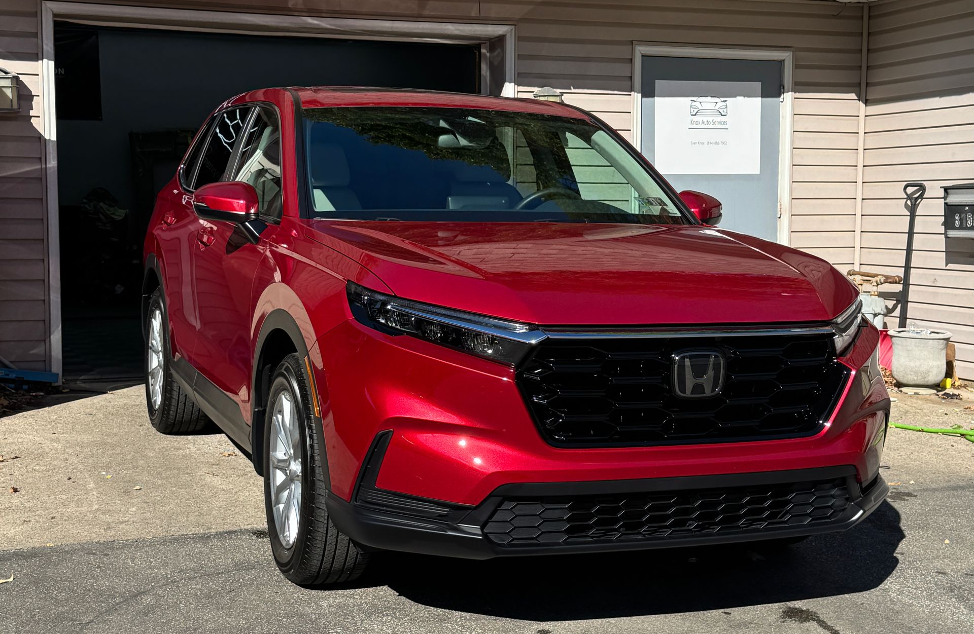 A worker in black gloves applies a liquid detailing product onto a blue sponge before a car’s glossy black exterior.