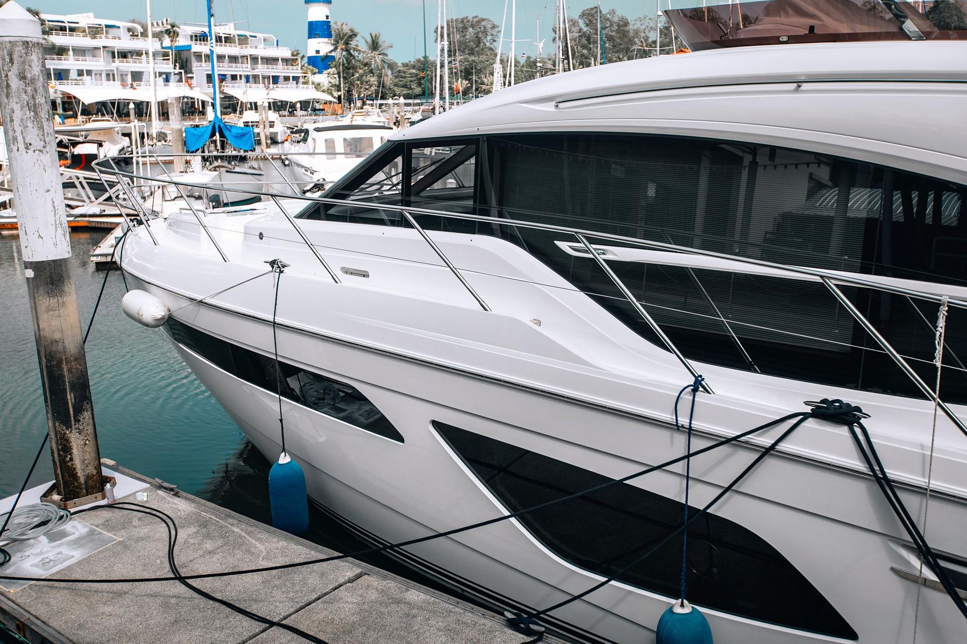 A sleek white yacht moored at a dock, featuring black hull accents and blue cylindrical fenders hanging from the side.