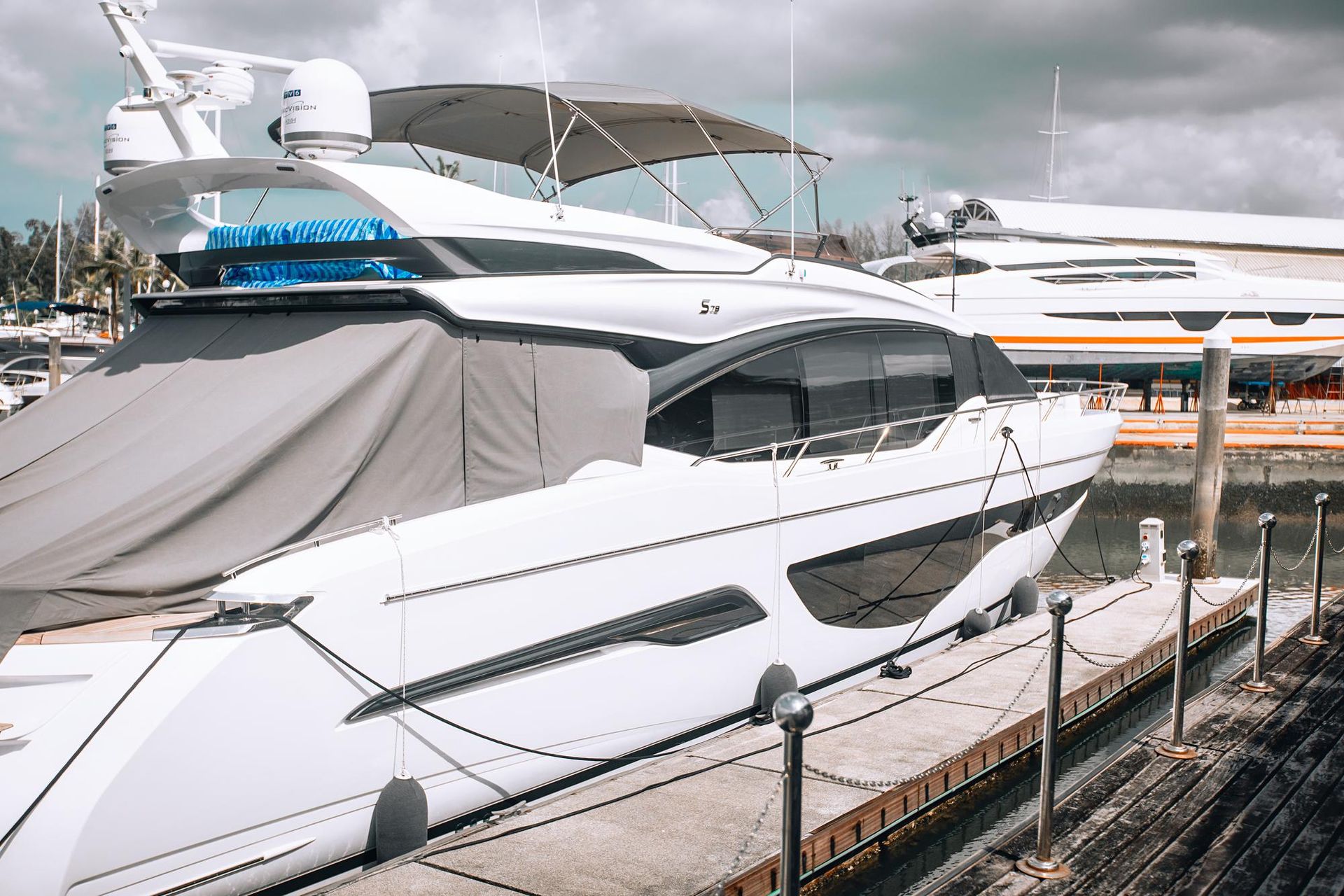 A white motor yacht docked at a marina, with a grey cover over its stern and a canopy above the deck.