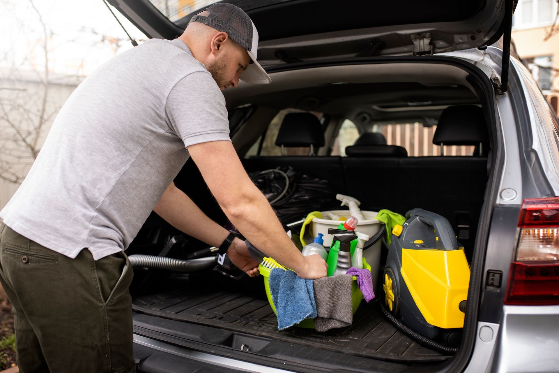 A person packing cleaning supplies and a yellow steam cleaner into the back of an open vehicle.