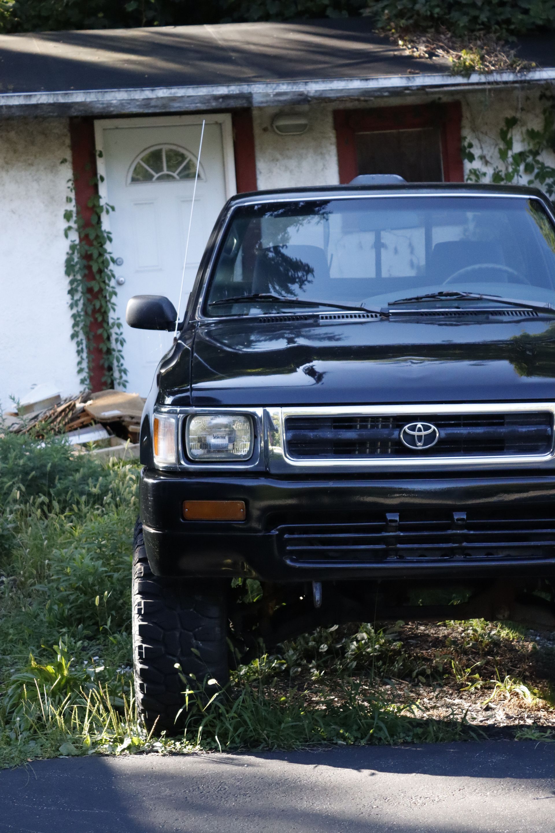 A black lifted Toyota pickup truck parked in front of a house with a white door.