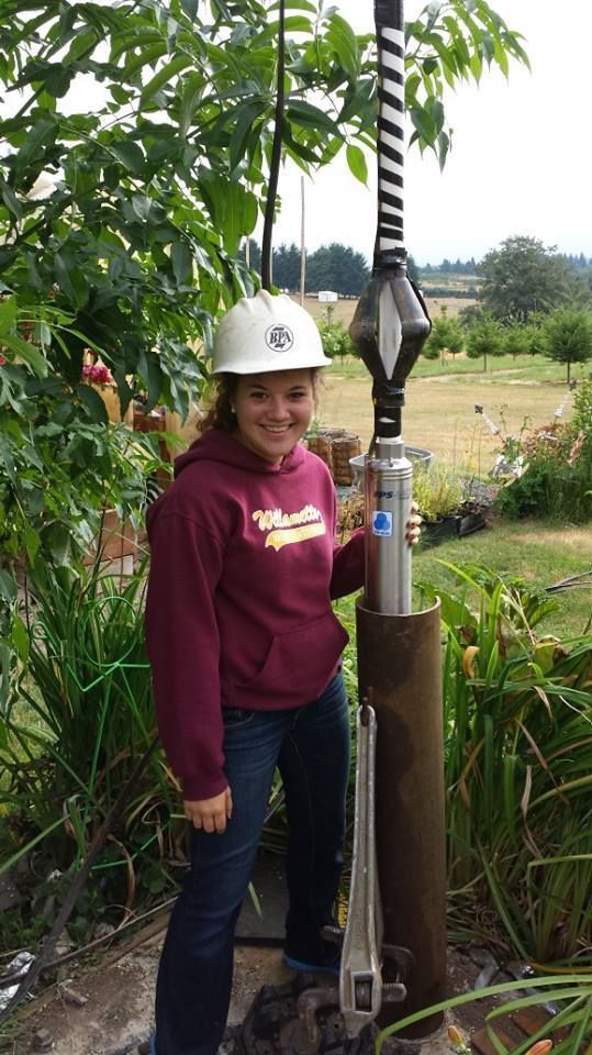 Woman in hard hat holding a drilling tool in a garden.