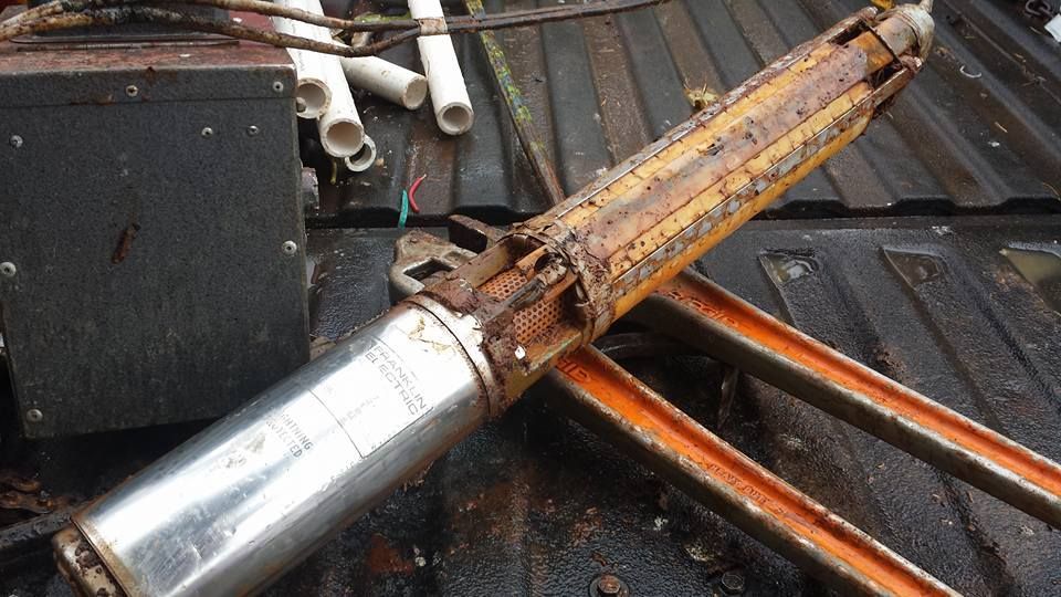 Rusty submersible water pump on a dirty metal surface, possibly a truck bed.