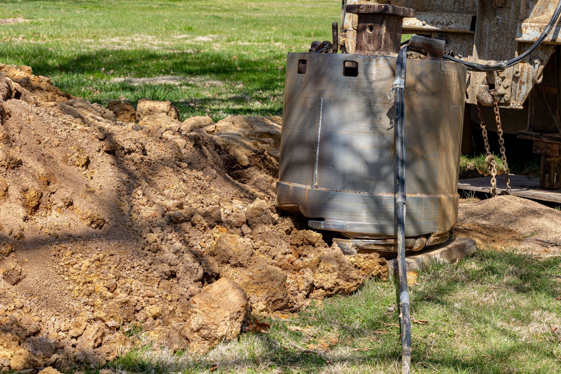 A drilling machine excavating dirt in a grassy area, with a pile of brown soil. A drilling machine excavating dirt in a grassy area, with a pile of brown soil.
