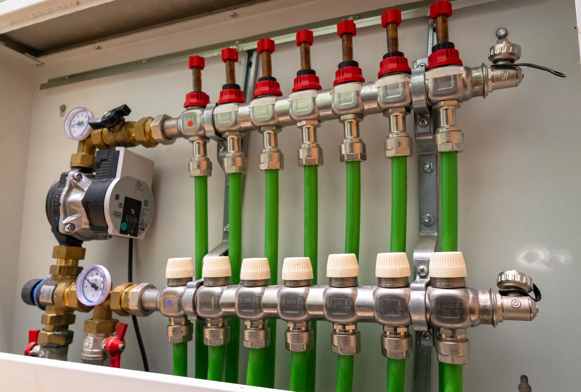 A wall-mounted radiant heating manifold system with pipes, valves, and a pump.