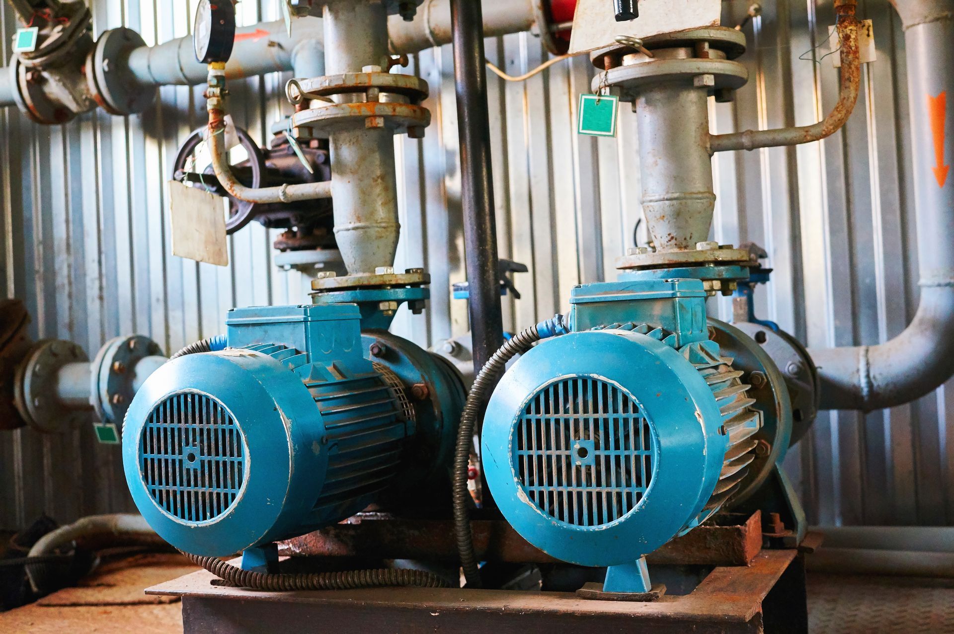 Two blue industrial pumps connected to pipes, in a room with corrugated metal walls.