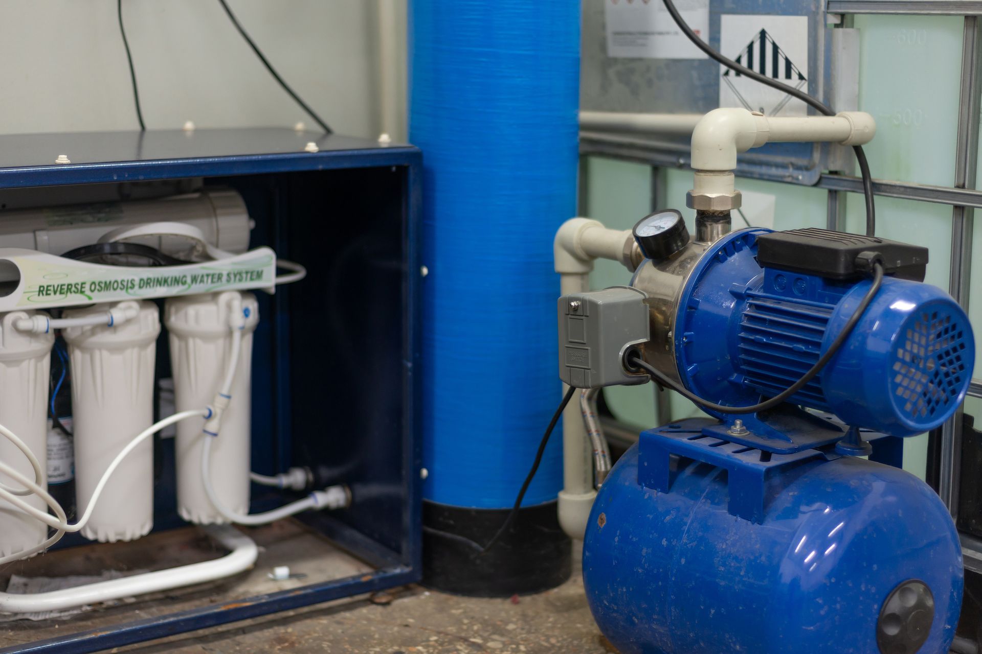 Water filtration system with filters, blue pump, and tank in an industrial setting.