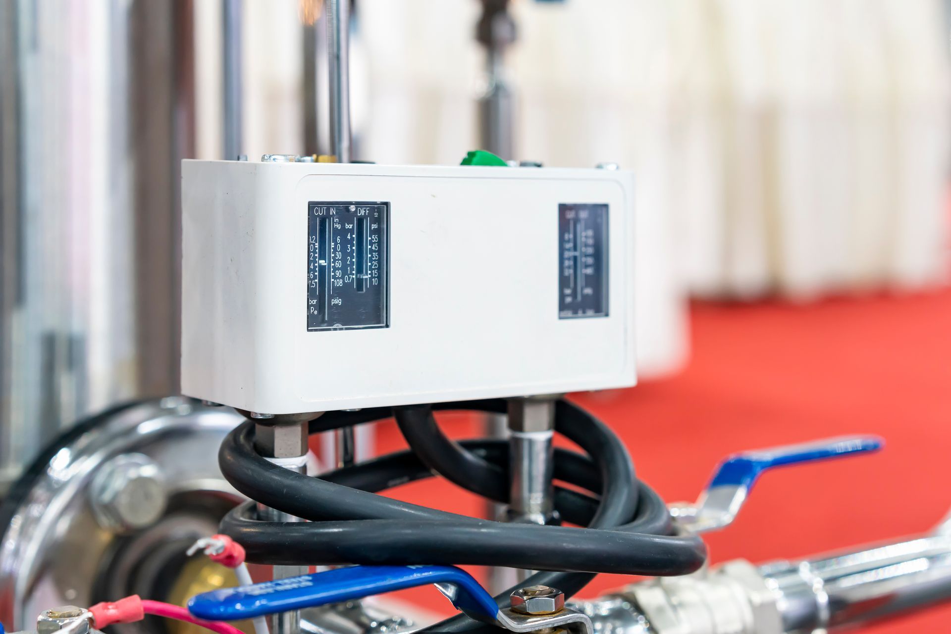 White control box with gauges and blue valve handles connected to a metal structure.