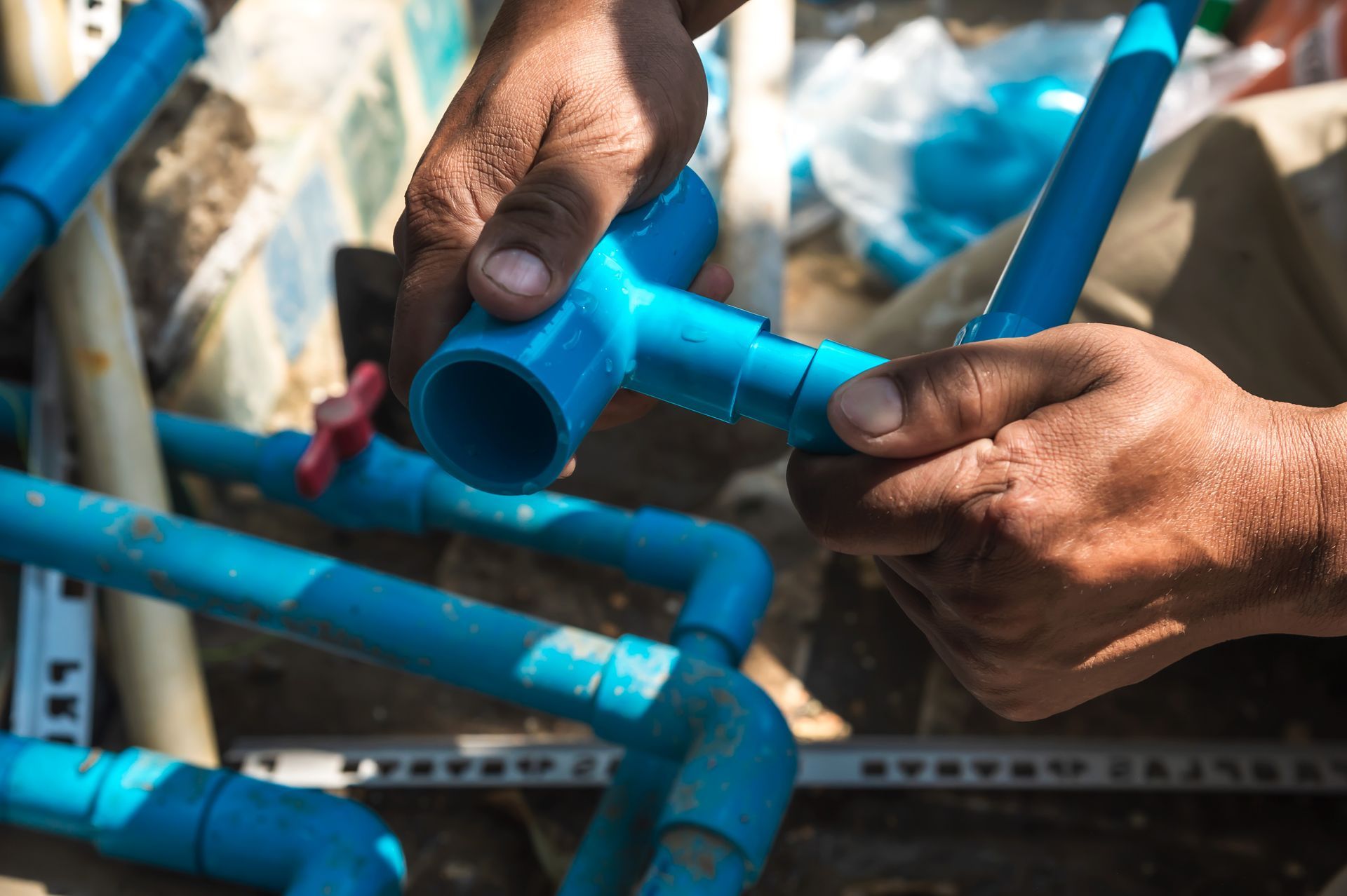 Hands connecting blue PVC pipes with a tee fitting.