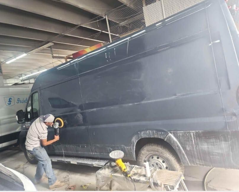 A man is polishing a black van in a garage.