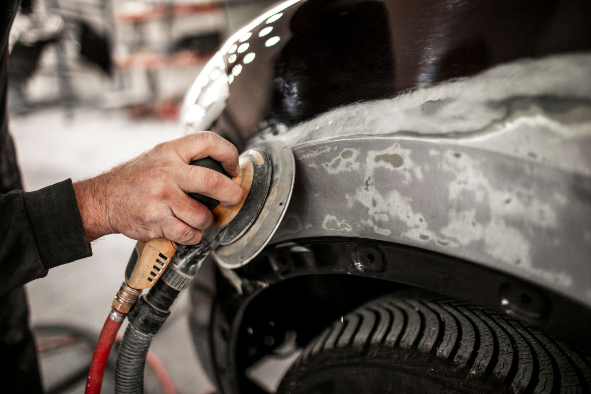 A man is sanding the fender of a car with an air sander.