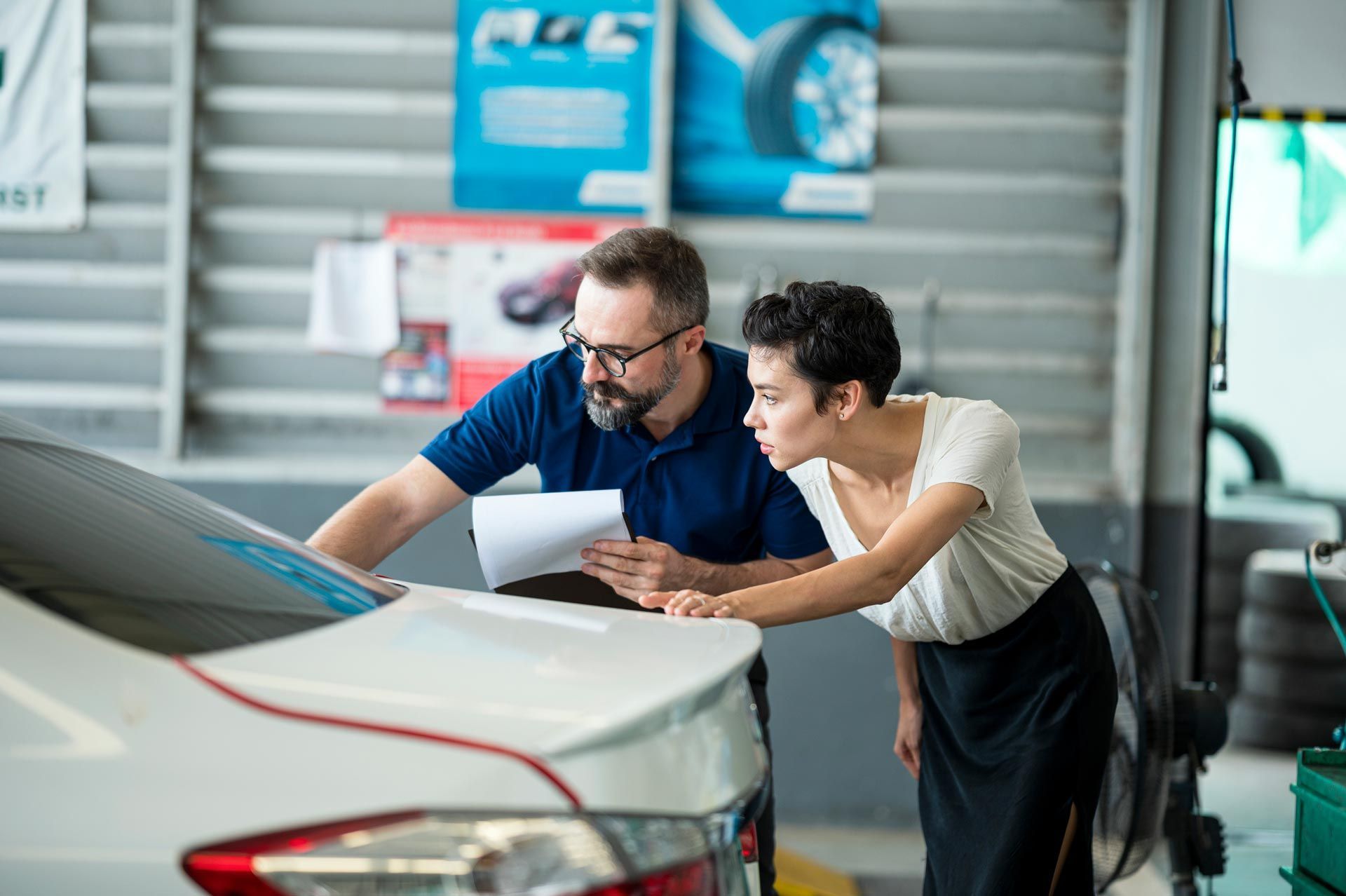 A man and a woman are looking at a car in a garage.