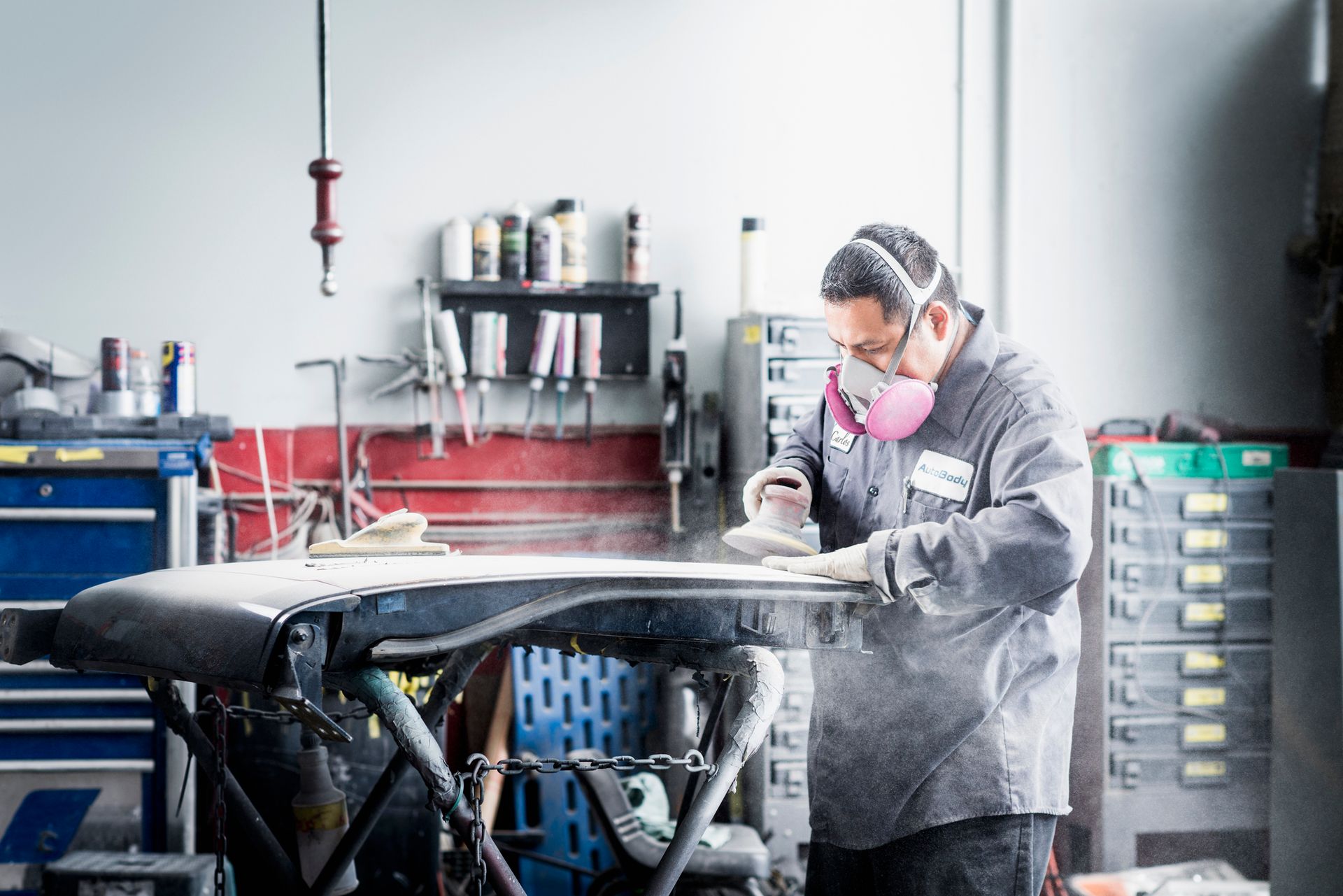 A man wearing a mask is sanding a piece of metal in a garage.