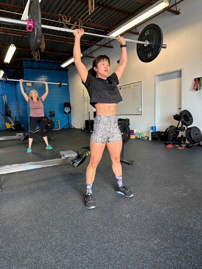 A woman is lifting a barbell over her head in a gym.