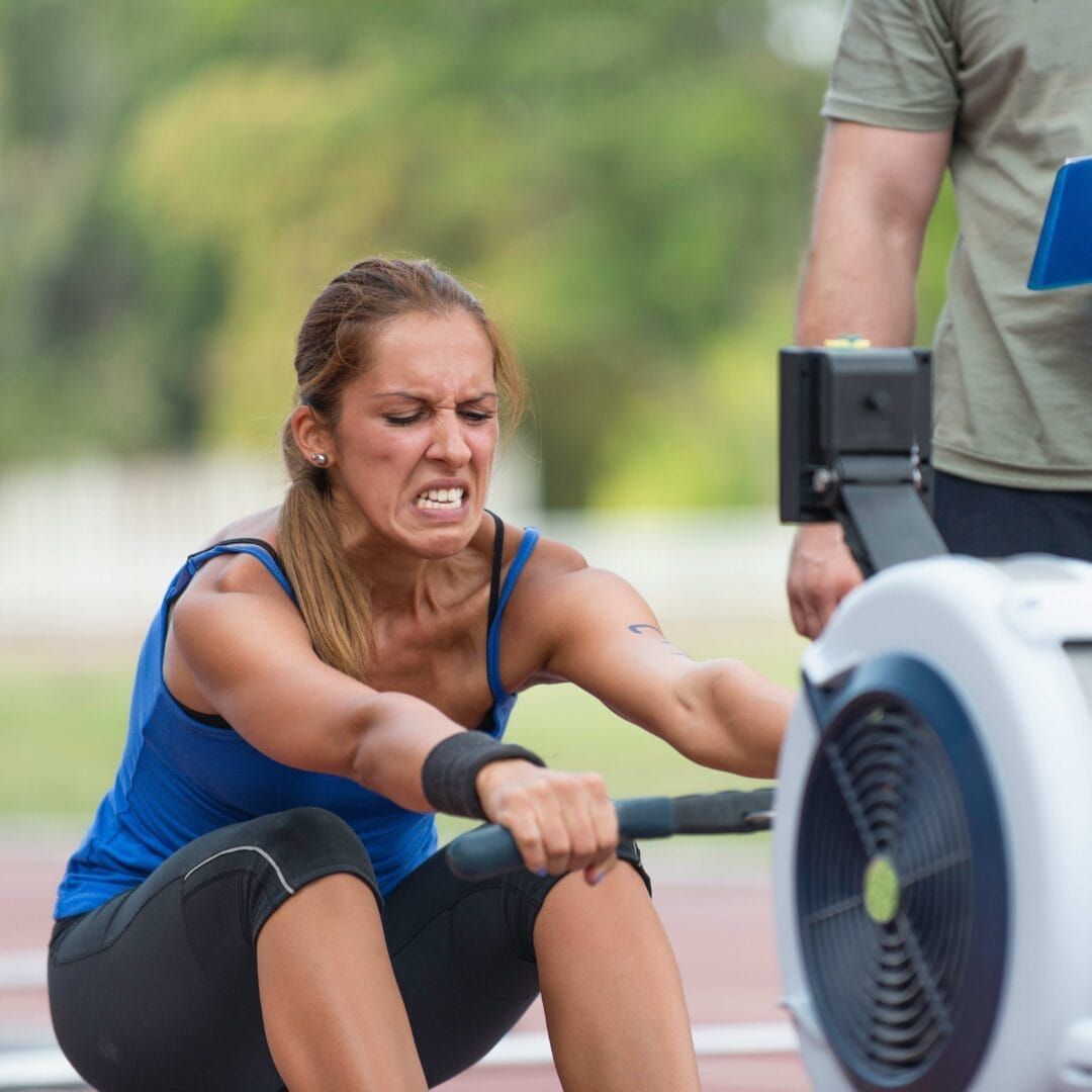 A woman is squatting down in front of a rowing machine