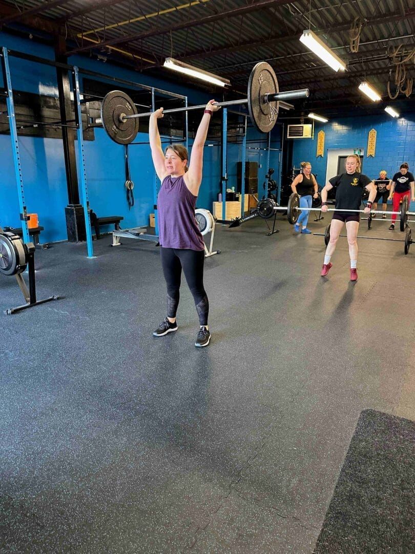 A woman is lifting a barbell over her head in a gym.