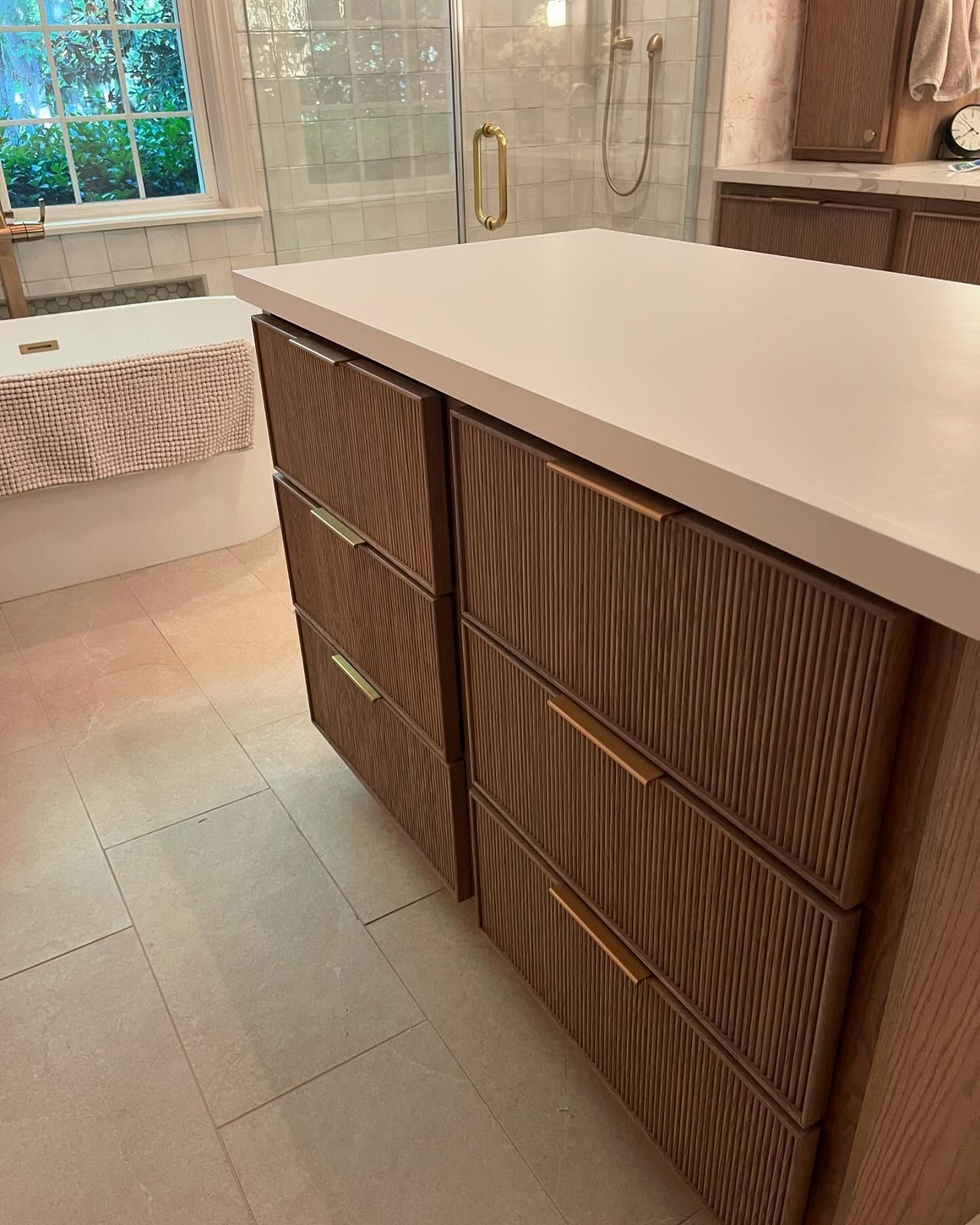 Bathroom island with wood-grain drawers, white countertop, gold hardware, and tiled floor.