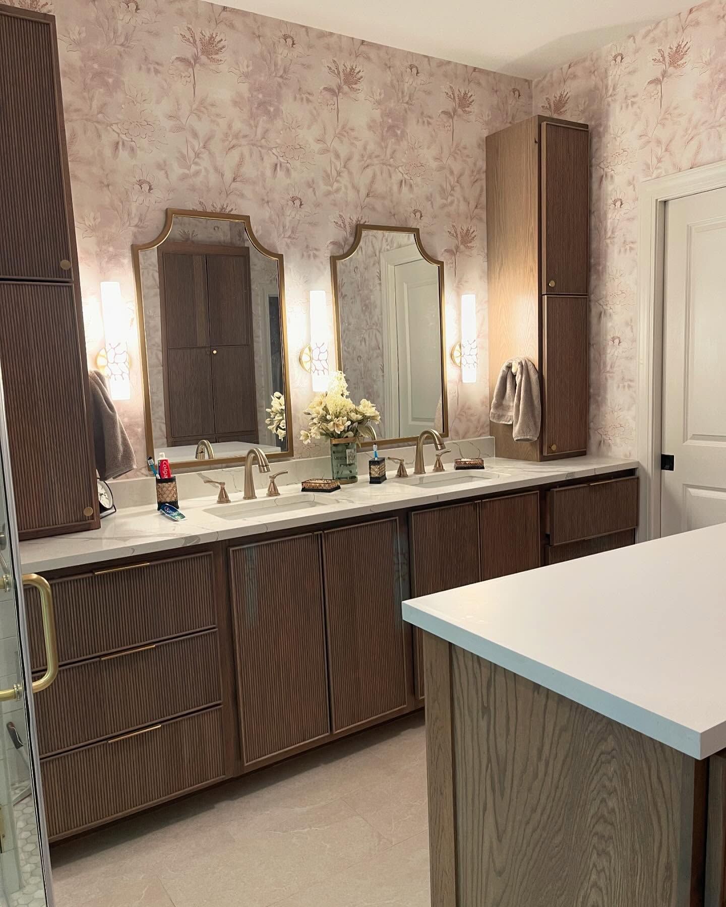 Bathroom with patterned wallpaper, double vanity, mirrors, and storage cabinets.