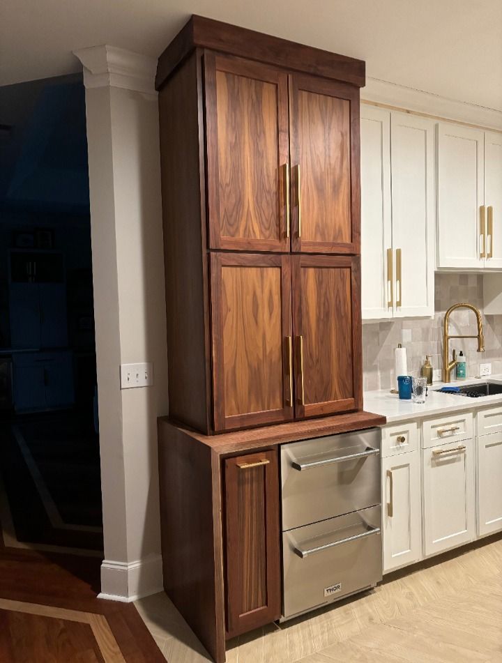 Tall, dark wood kitchen cabinet with gold handles, adjacent to white cabinets and stainless steel dishwasher.