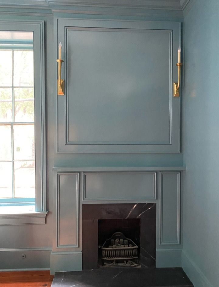 Blue painted fireplace with black marble hearth and brass sconces. Next to a window.