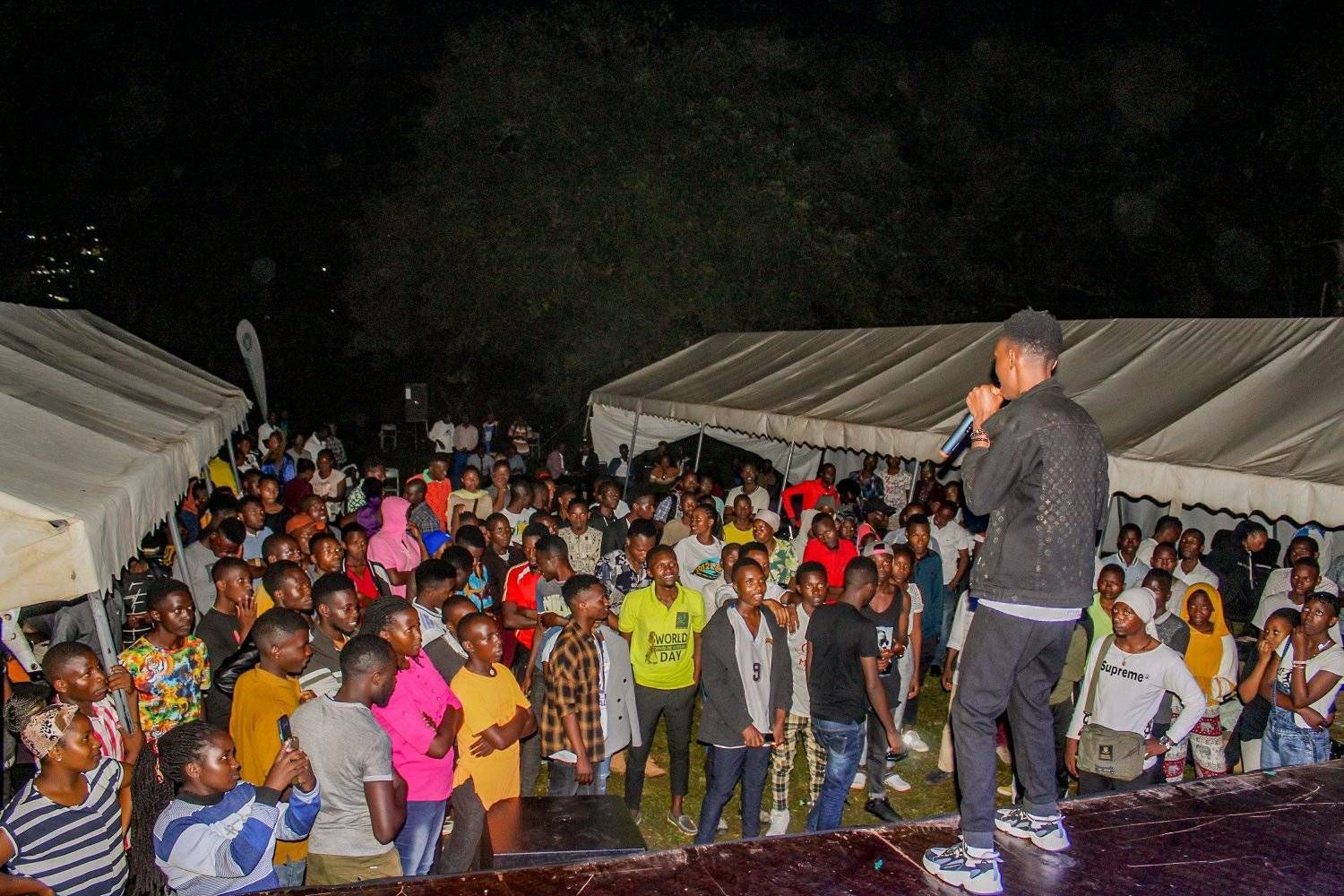 A man is standing on a stage holding a microphone in front of a crowd of people.