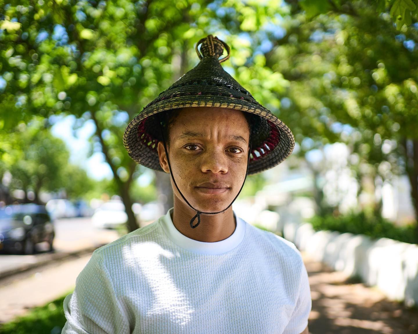 A young man wearing a hat and a white sweater is standing on a sidewalk.