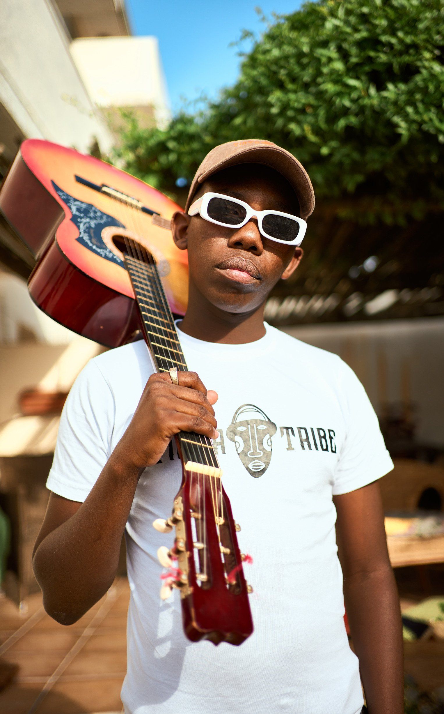 A man wearing sunglasses is holding a guitar on his shoulder.