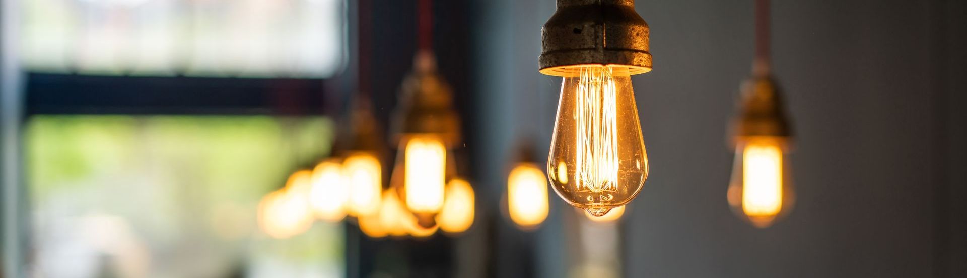 Gros plan sur des ampoules allumées suspendues au plafond. Une douce lueur orangée se détache sur un fond flou.