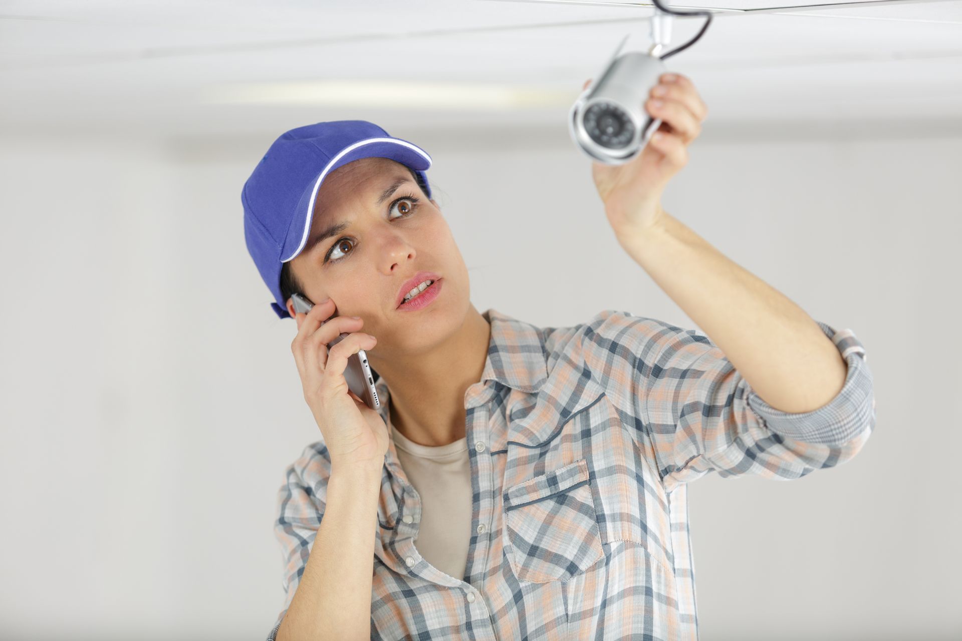 Une femme parle au téléphone portable tout en réparant une caméra de sécurité.