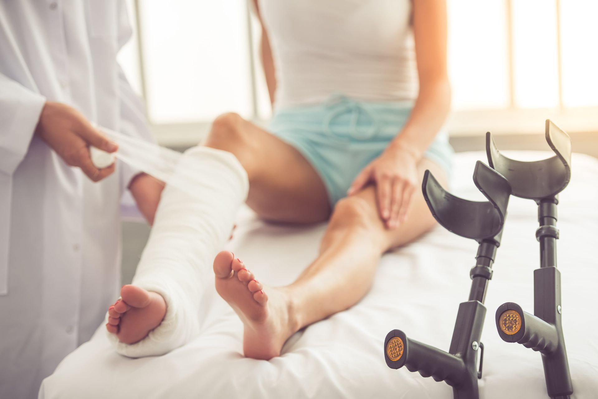 A woman with a cast on her leg is sitting on a bed with crutches.