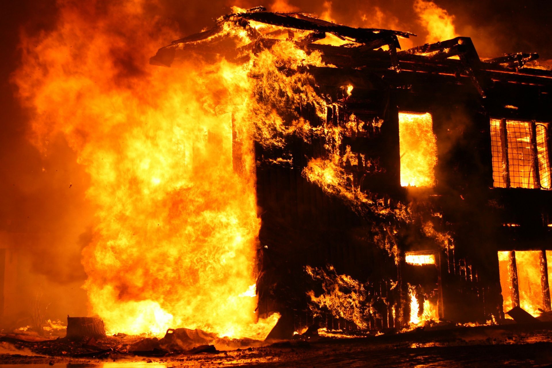 A two-story building engulfed in bright orange flames and thick smoke at night.