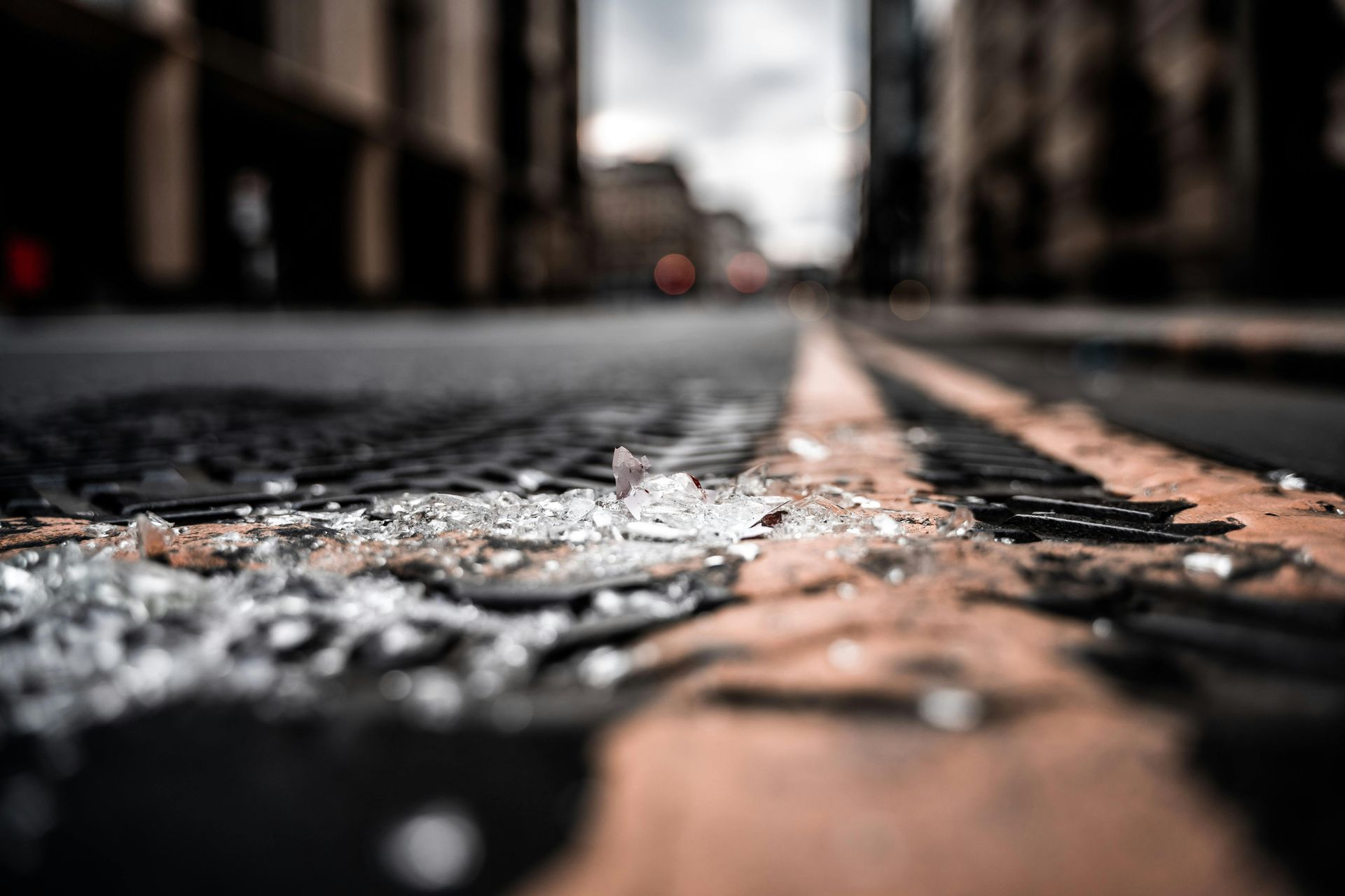 Shards of broken glass lie scattered on a dark city street, with blurred buildings in the background.