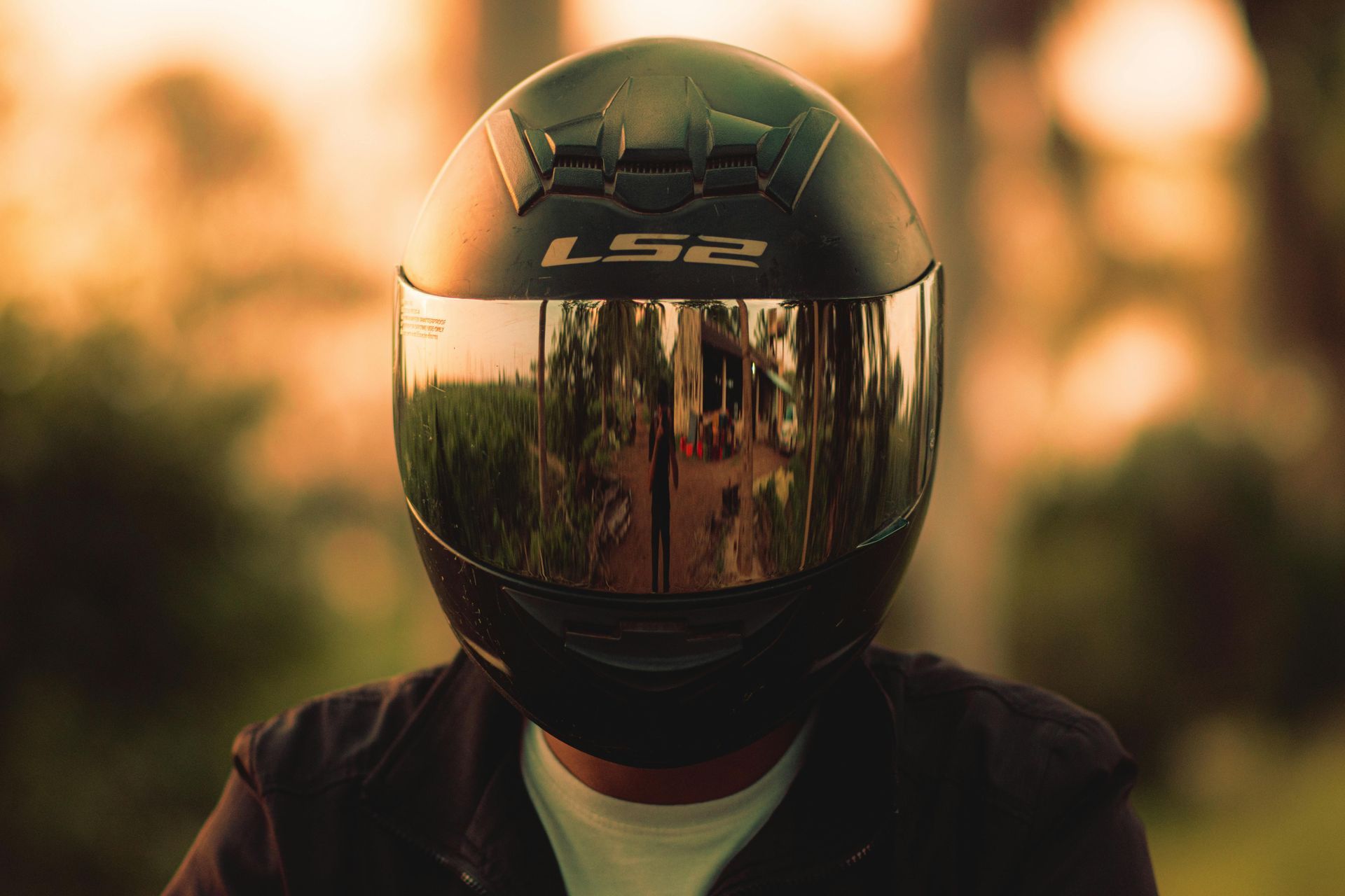 A person wearing a black LS2 motorcycle helmet with a reflective visor, set against a blurred, warm-toned outdoor background.