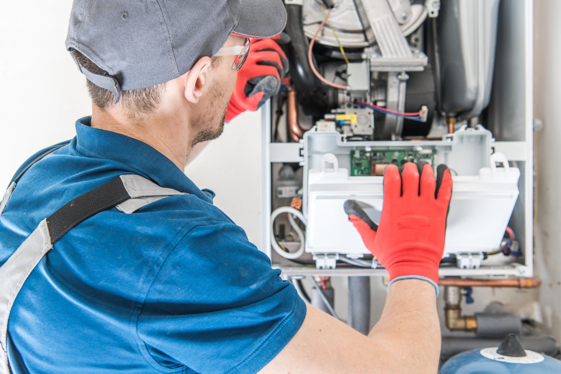 Technician in blue uniform and red gloves repairing an open electrical unit with wires exposed