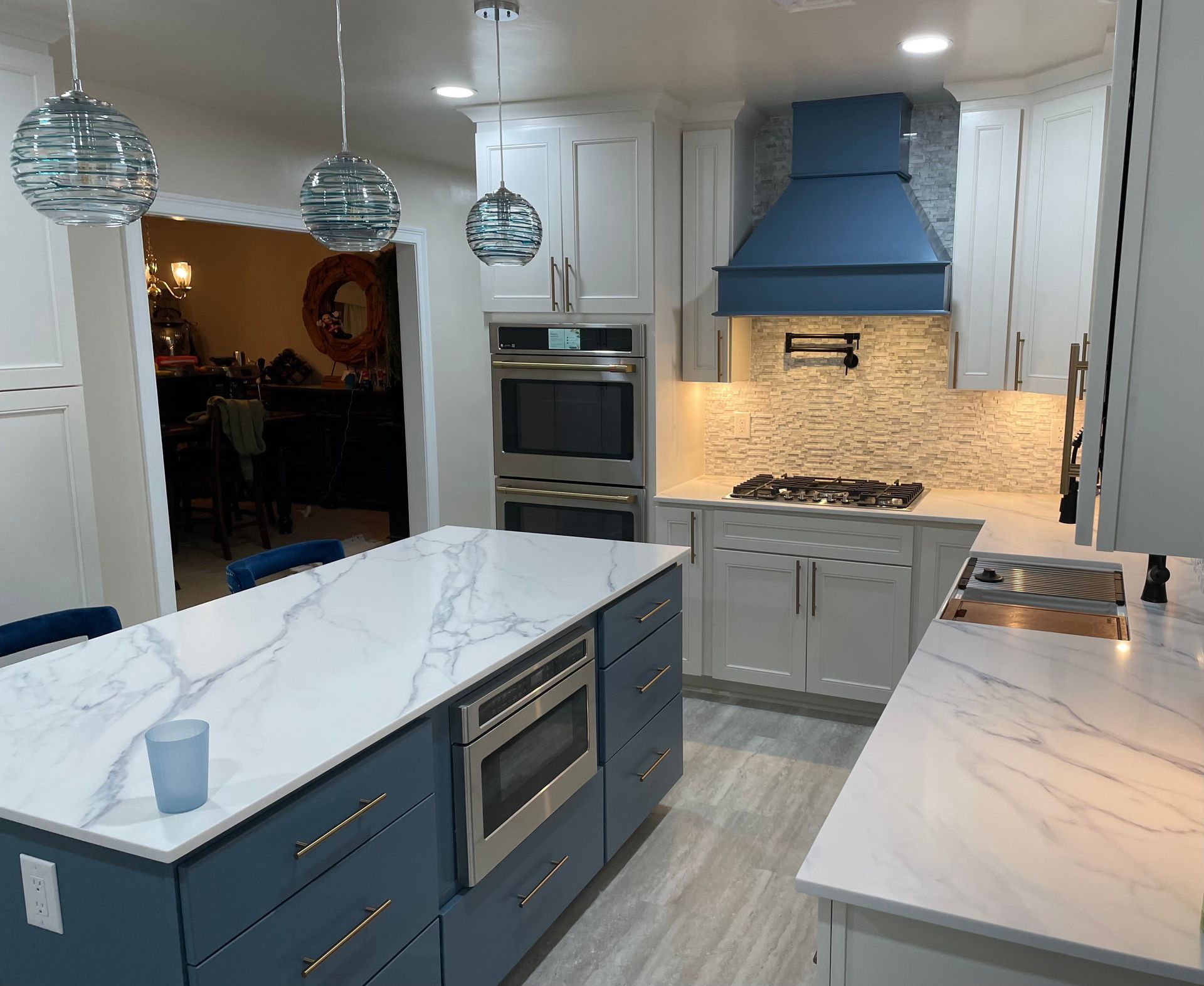 Modern kitchen with blue island, white cabinets, and marble countertops.