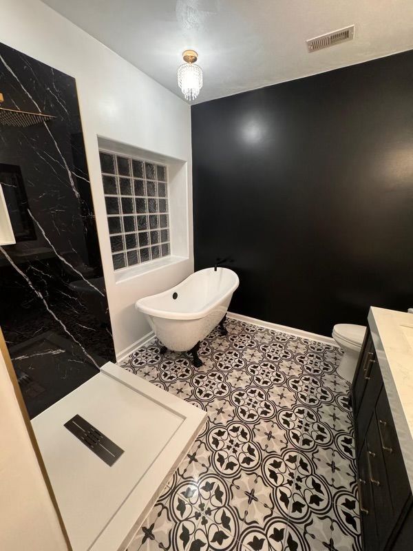 Modern bathroom with black and white tile floor, black accent wall, clawfoot tub, and marble shower.