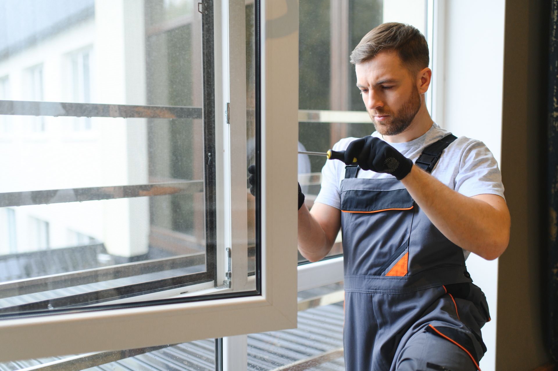Man in overalls installing a window, interior setting.