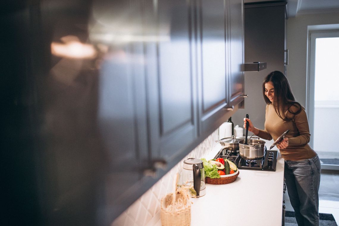 A woman is cooking in a kitchen and looking at her phone.