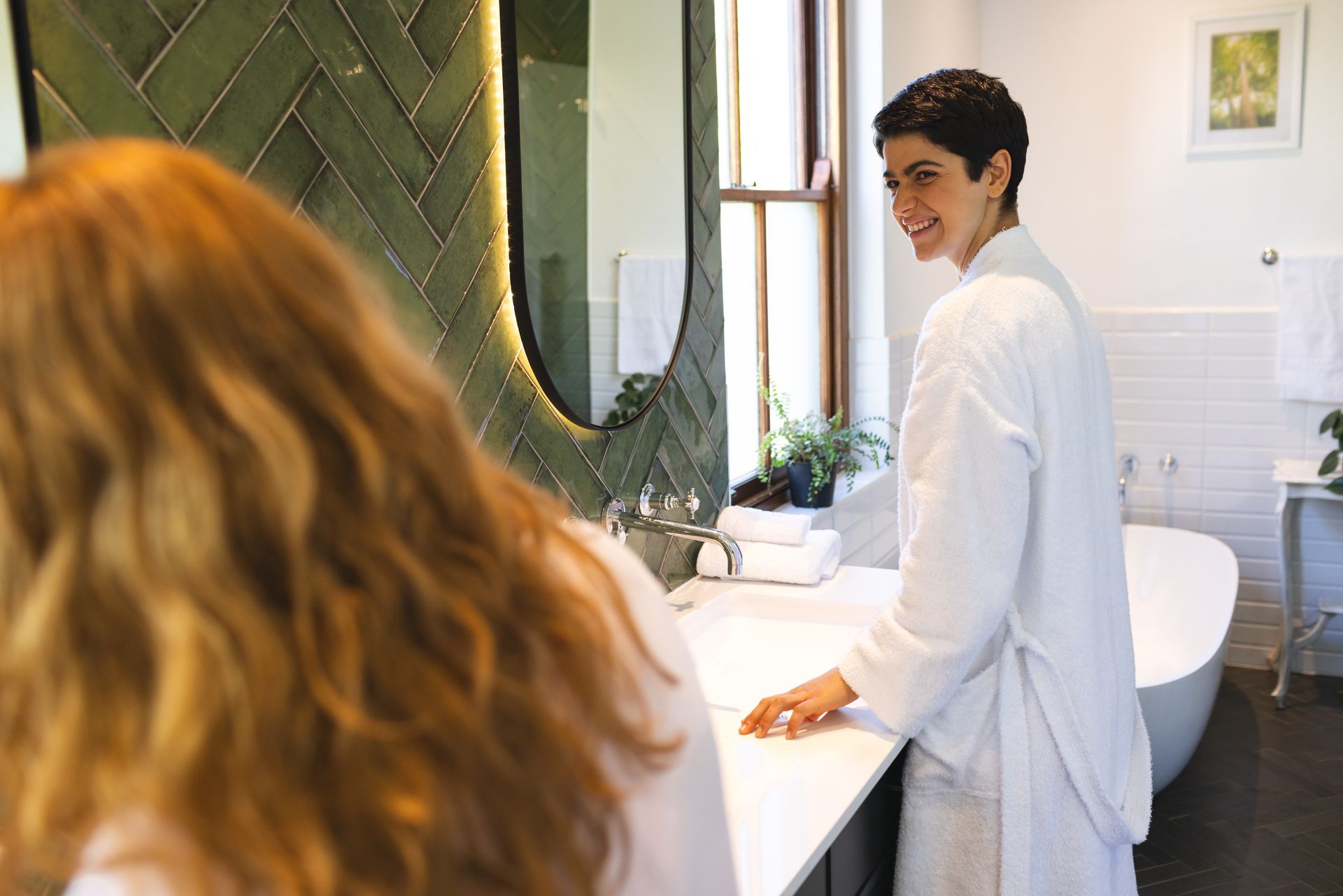 A woman in a bathrobe is standing next to another woman in a bathroom.