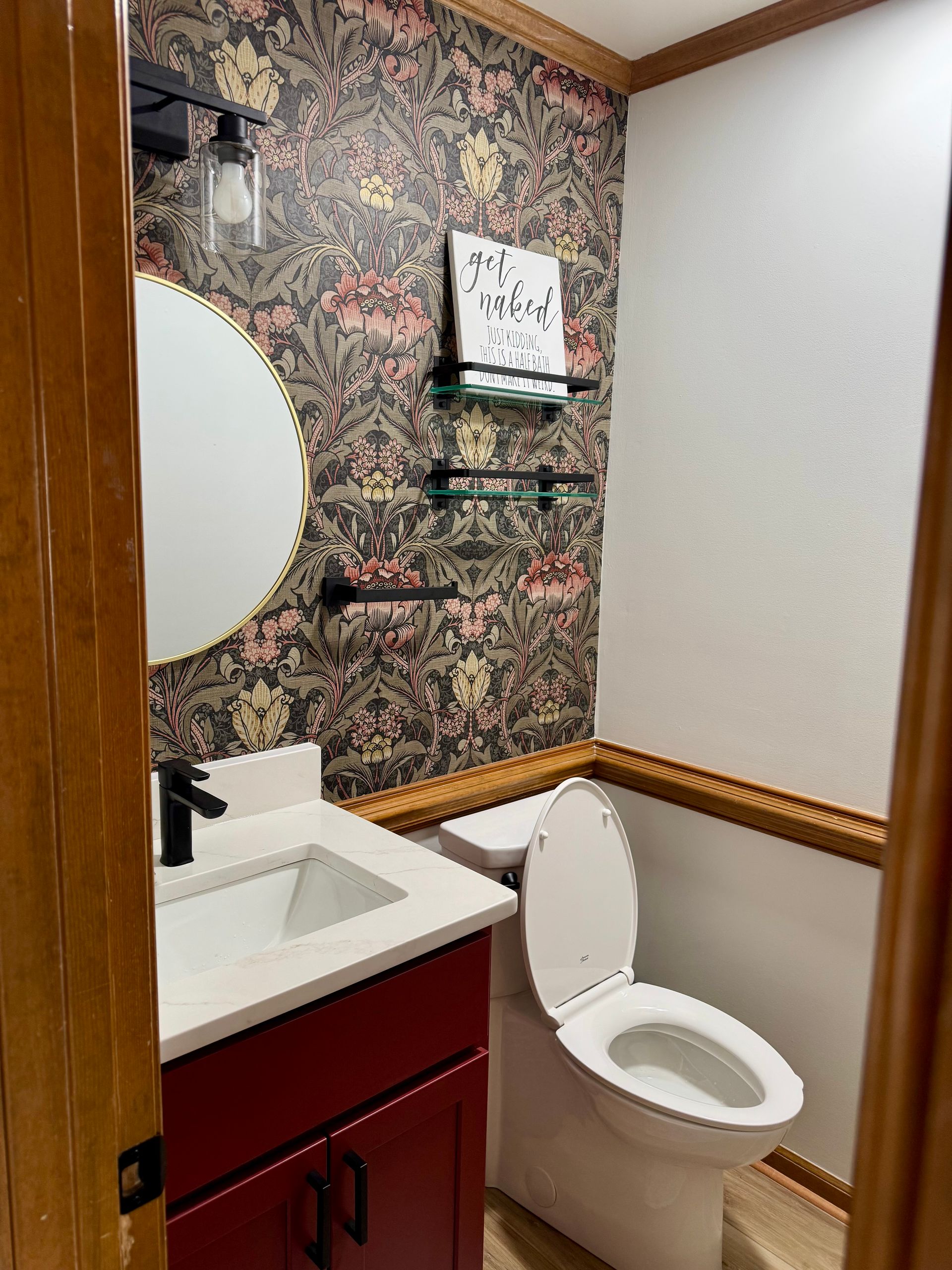 A bathroom with a toilet , sink , mirror and floral wallpaper.