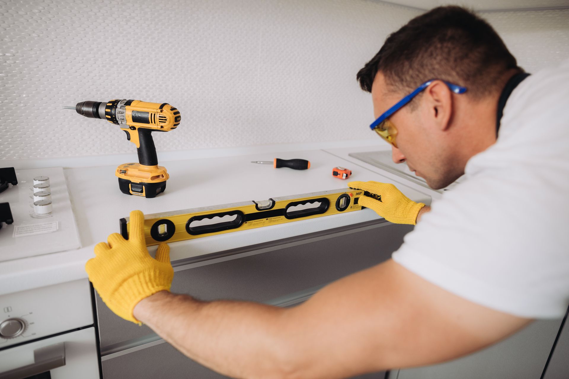 A man is measuring a cabinet with a level in a kitchen.