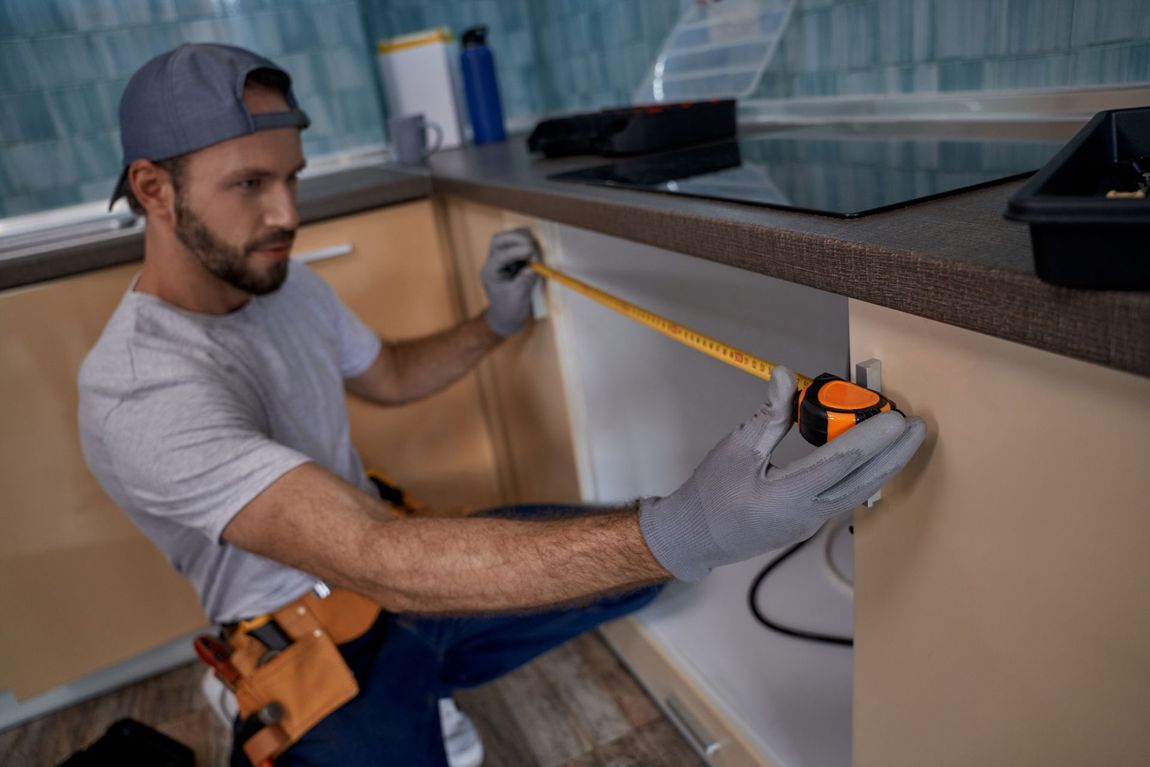 A man is measuring a cabinet with a tape measure in a kitchen.