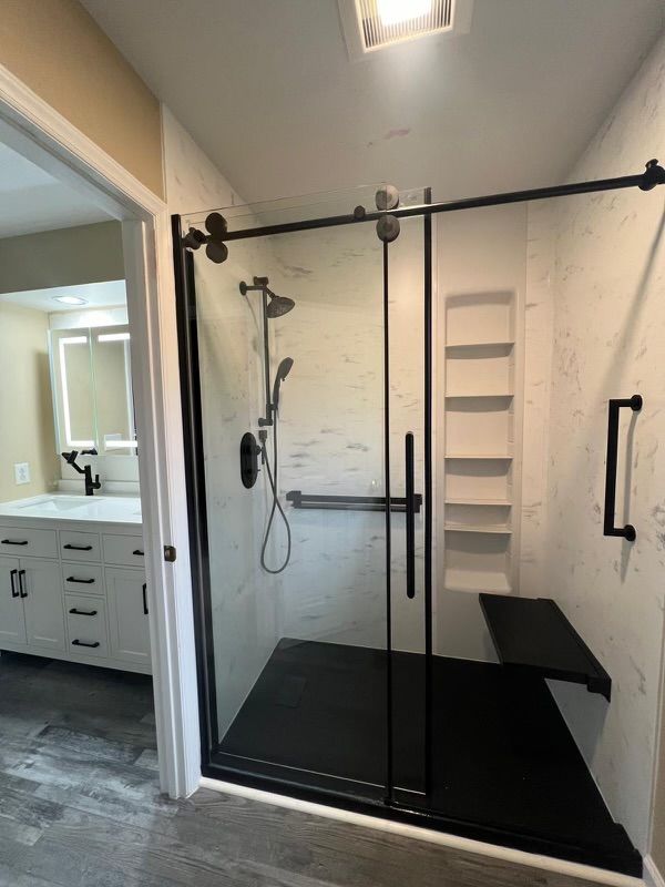 A bathroom with a sliding glass shower door and a black bench.