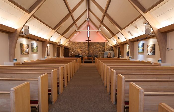 The inside of a church with rows of wooden benches and a stained glass window.