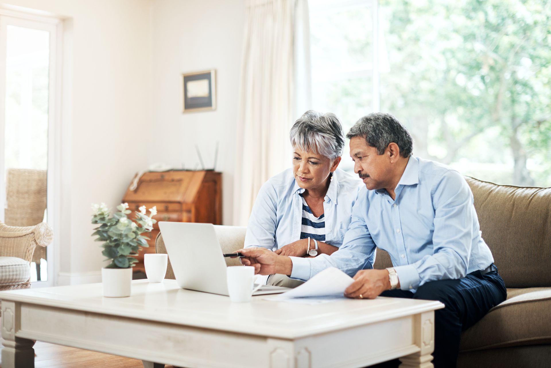 a man and a woman are sitting on a couch looking at a laptop .