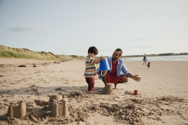 A man and a child are playing in the sand on the beach.