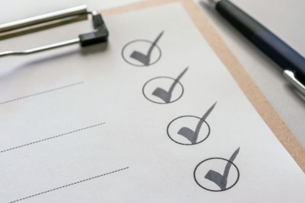 A clipboard with four check marks on it next to a pen.