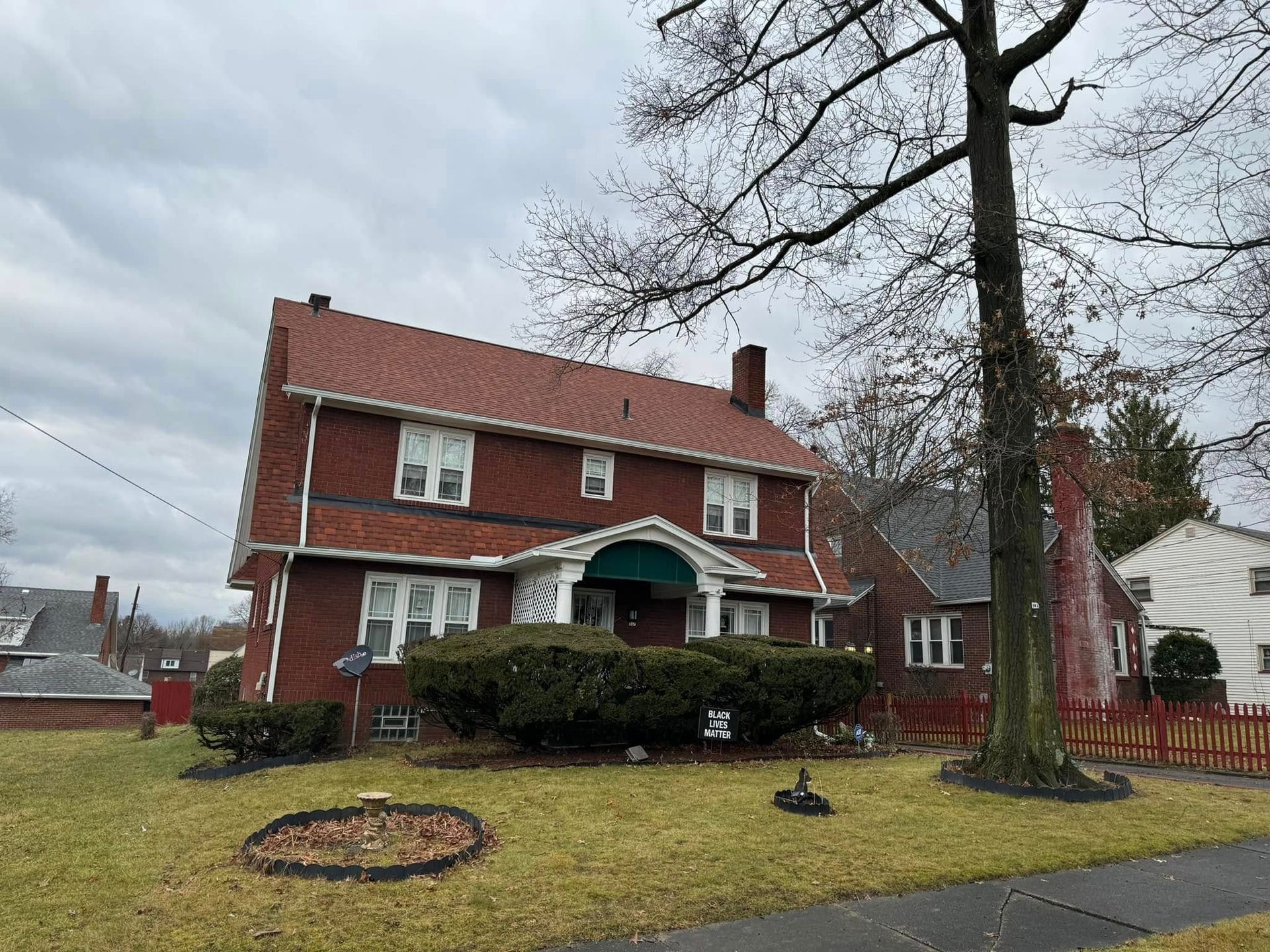 Red brick house with green porch and large tree on a cloudy day