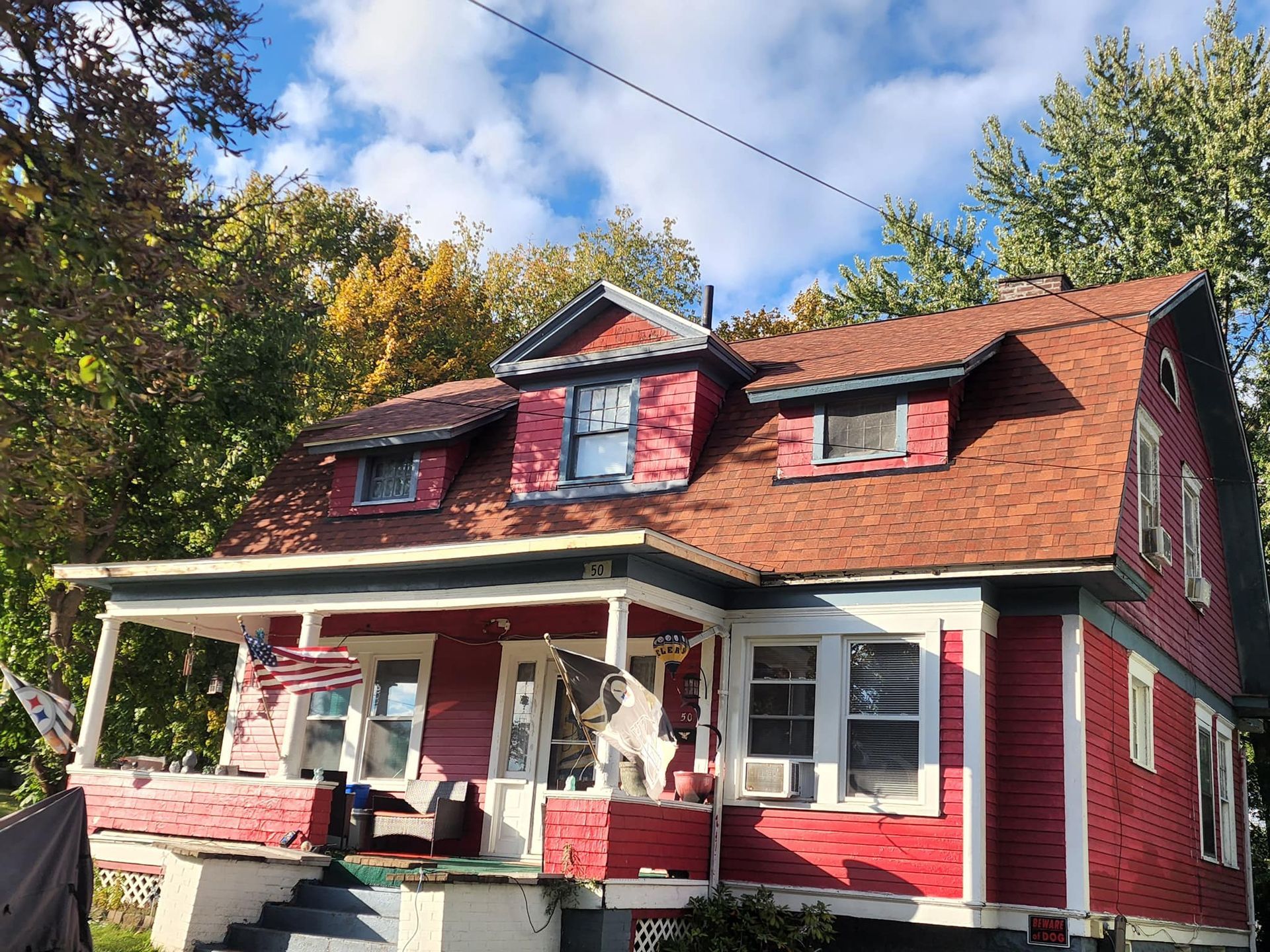 Red two-story house with white porch and dormer windows under a blue sky